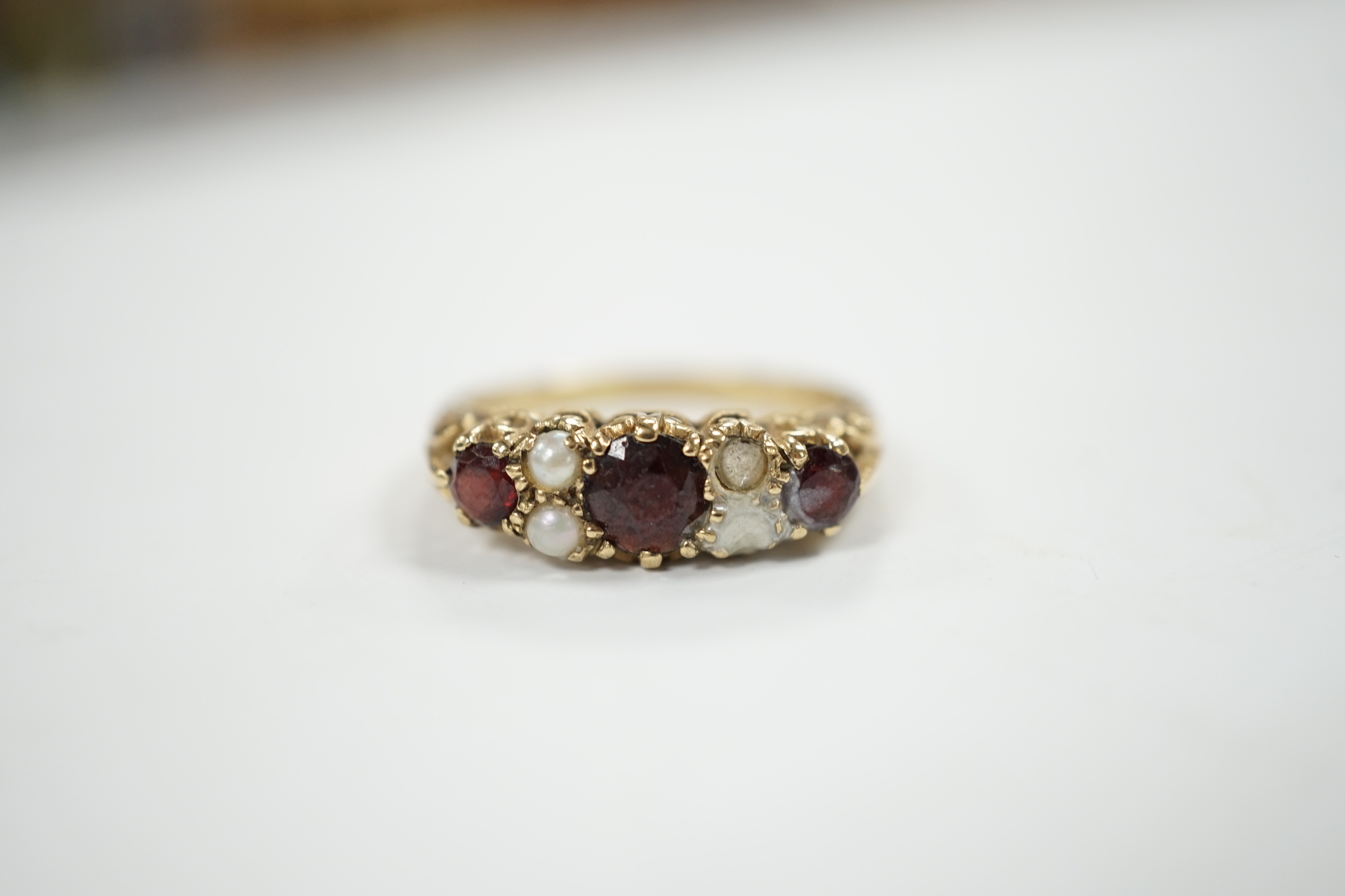 A modern 9ct gold, three stone garnet and four stone split pearl set half hoop ring (two pearls missing), size S/T, gross weight 3.8 grams.